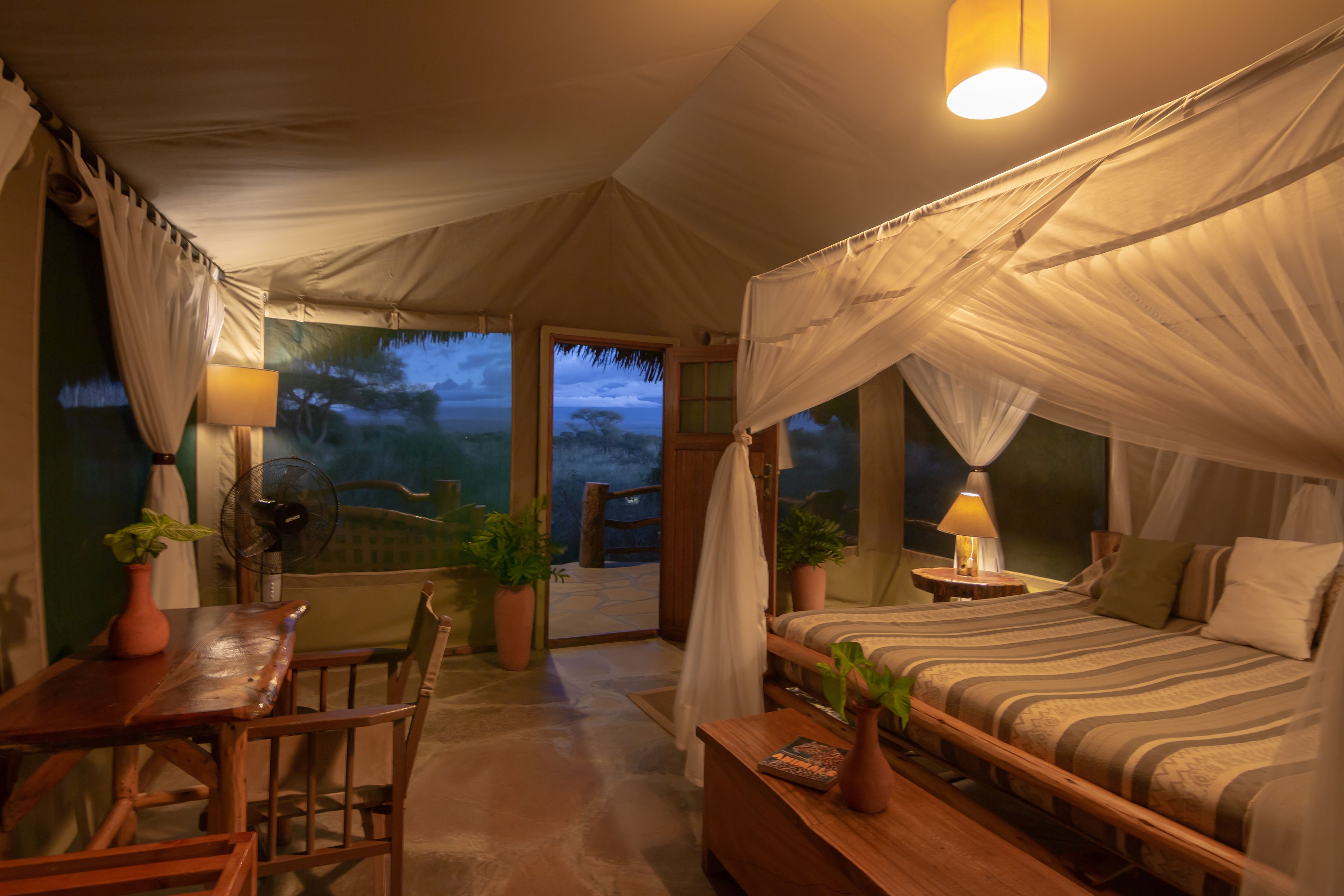 Ein Zelten-ähnlicher Raum mit Bett, Nachttisch, Lampe und Blumentöpfen.
