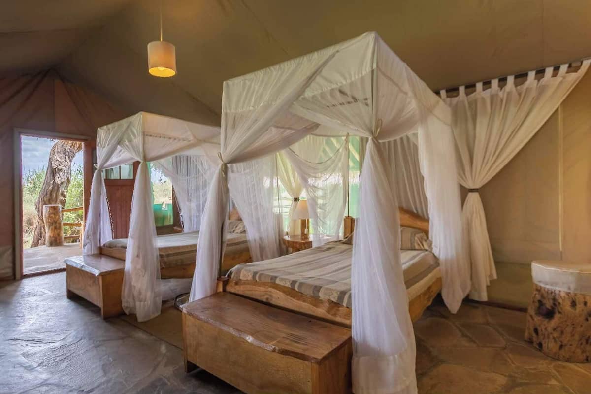 Ein Zimmer mit zwei hölzernen Betten, jedes mit Baldachin, und einem Steinboden.