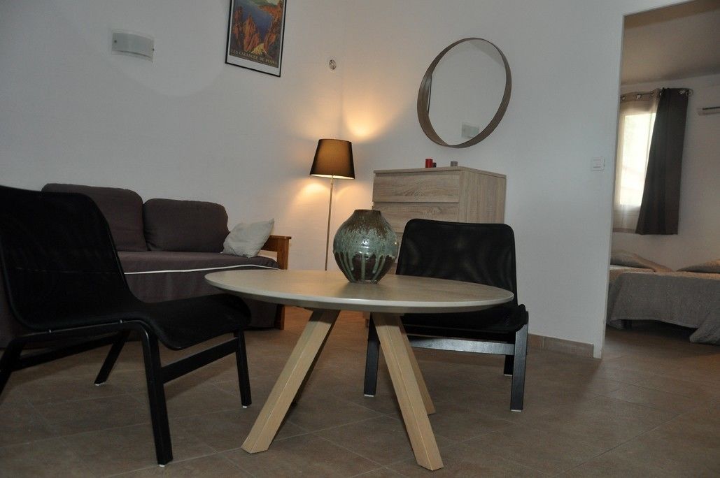 Een woonkamer met een ronde tafel, twee zwarte stoelen, een bank, een lamp, een spiegel en een dressoir.