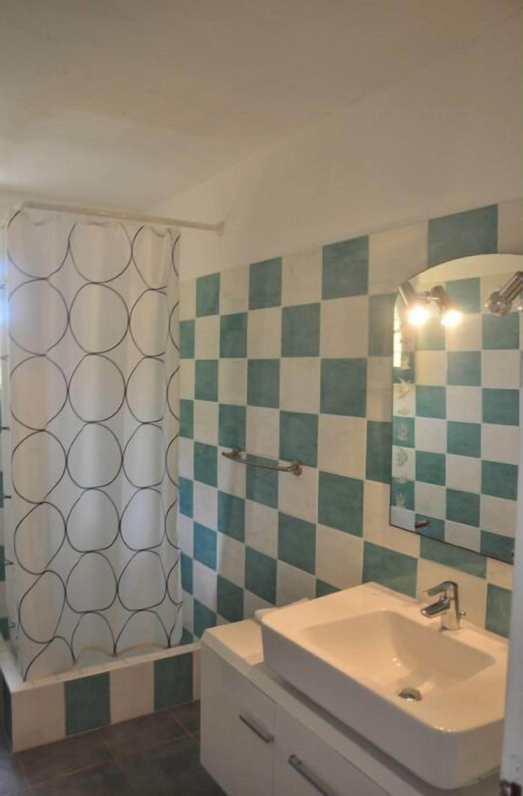 Ein Badezimmer mit Wandfliesen im Schachbrettmuster, einem weißen Waschbecken und einem Duschvorhang mit kreisförmigem Muster.