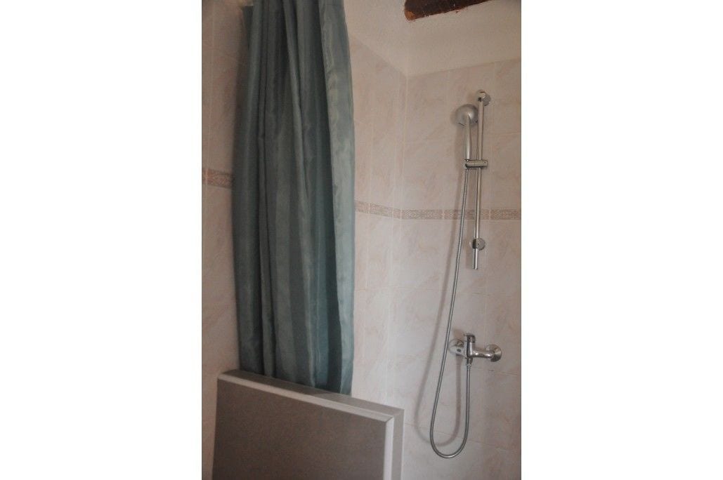 A shower with a curtain, a handheld showerhead, and a wall-mounted faucet.