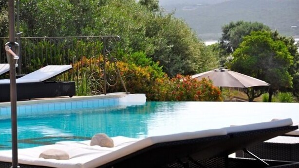 A poolside area with lounge chairs and a view of the sea. - Résidence Maora Village (Bonifacio)