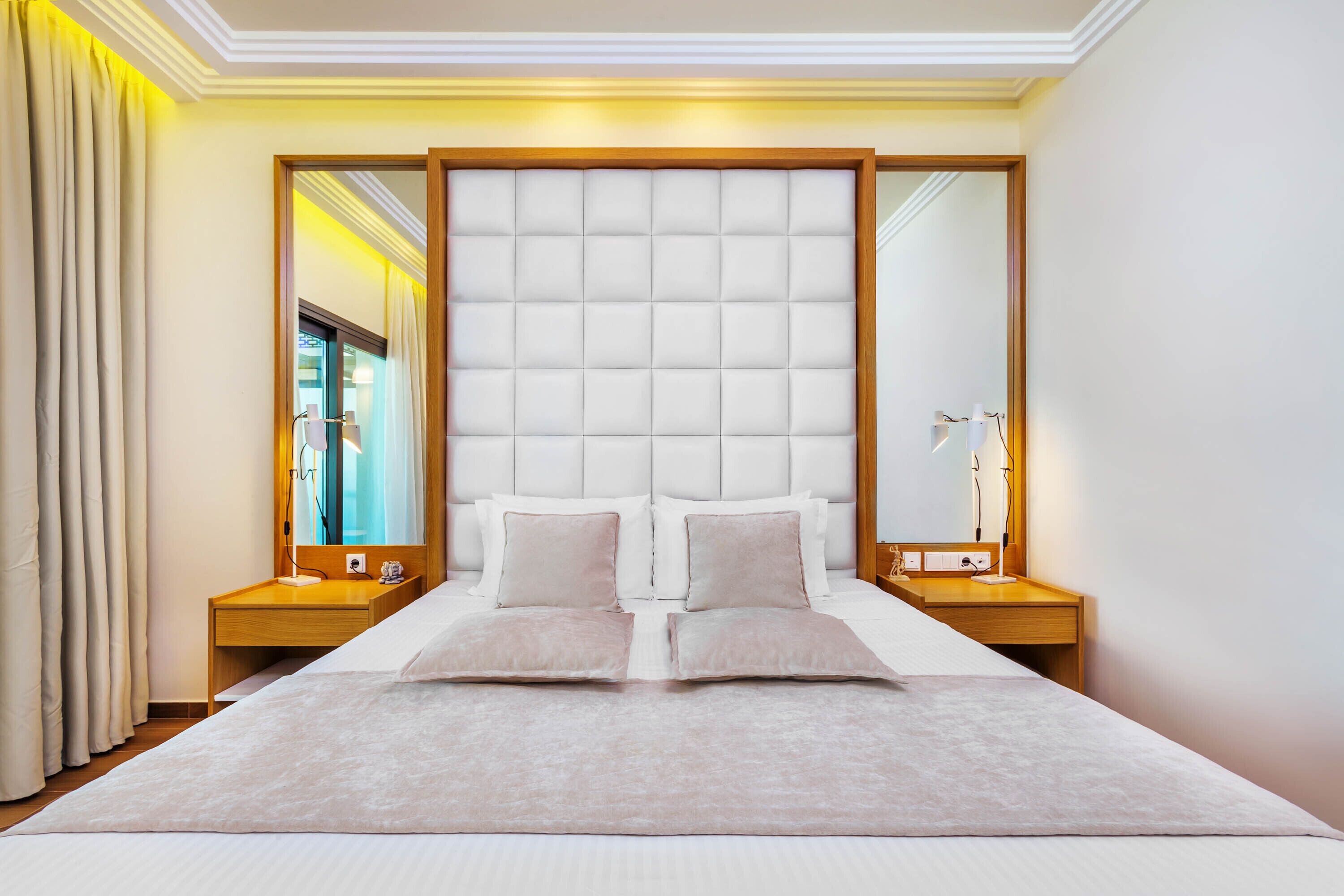 A modern bedroom with a large bed, two bedside tables, a headboard, and a mirror.