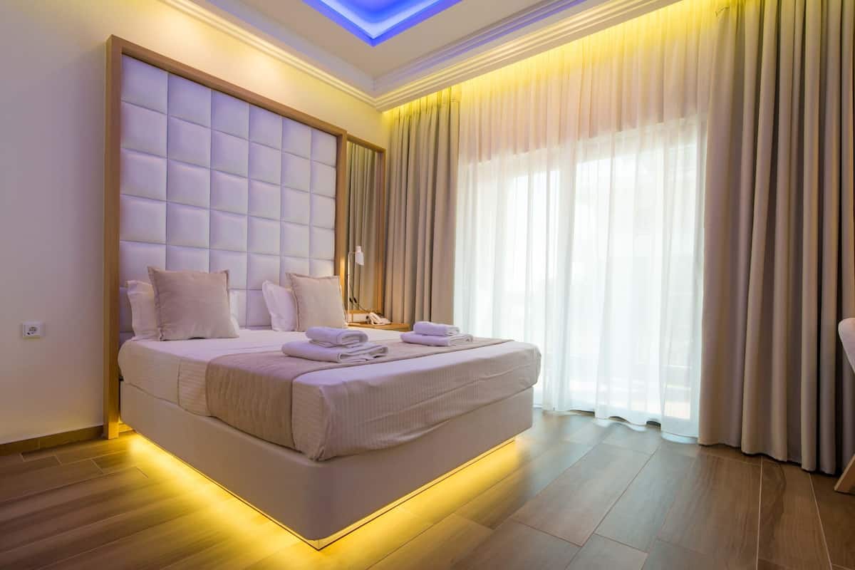A modern bedroom with a large bed, a ceiling light, and a view of the outside through sheer curtains.