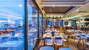 Restaurante moderno com vista para a cidade através de amplas janelas.