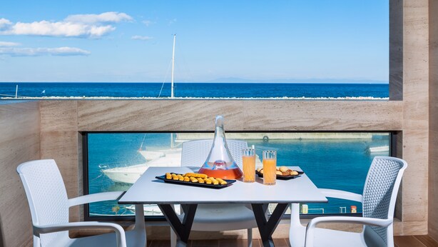 Uma mesa com uma bebida, um prato de comida e um copo de suco de laranja numa varanda com vista para o mar.