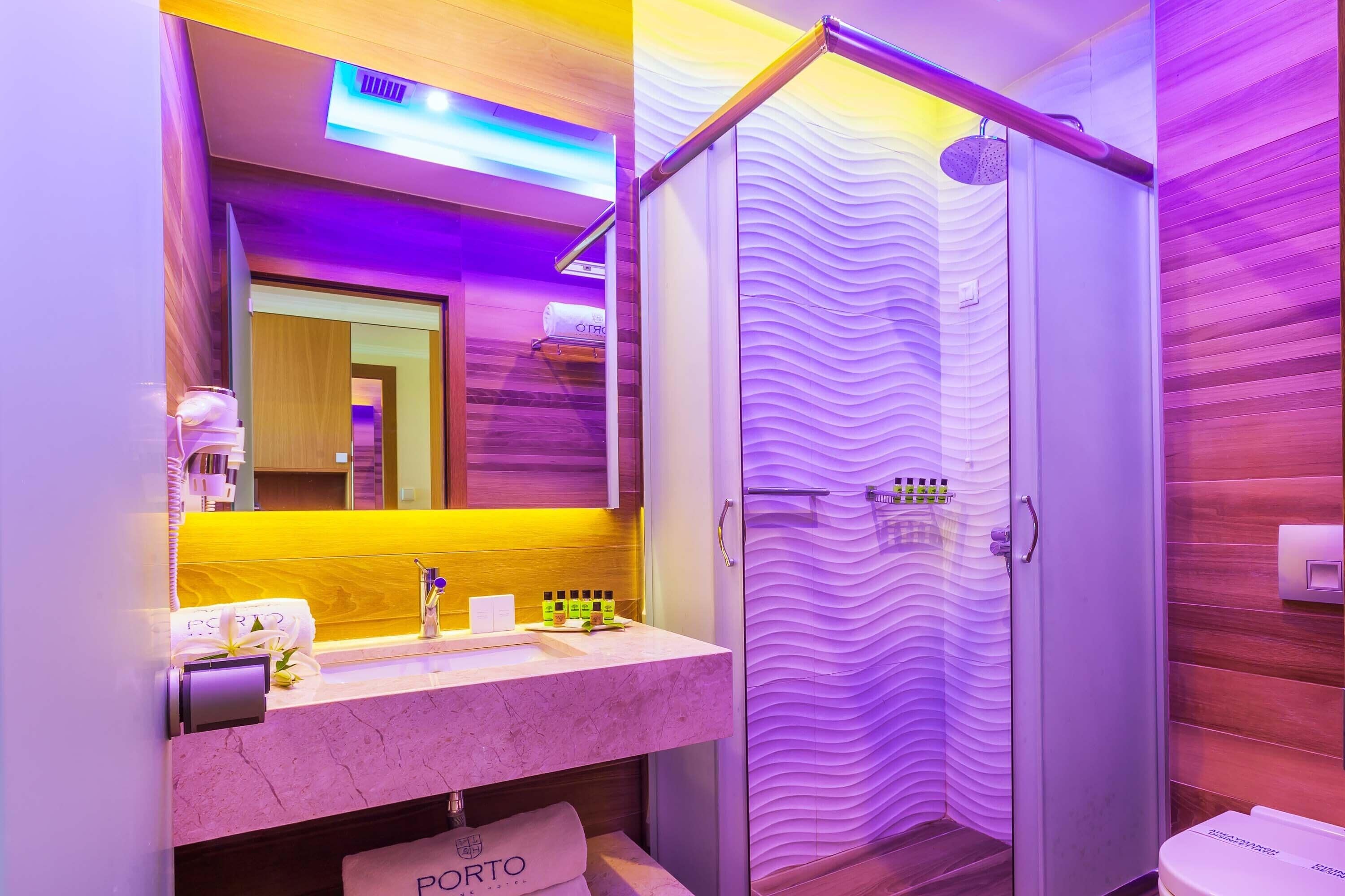 Een moderne badkamer met een marmeren wastafel, een spiegel, een douche met een golfvormige glazen deur en een houten wand.