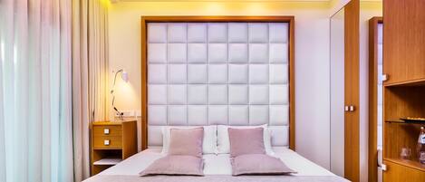 Una habitación de hotel moderna con una cama grande, una mesita de noche de madera, una lámpara de noche y un armario.