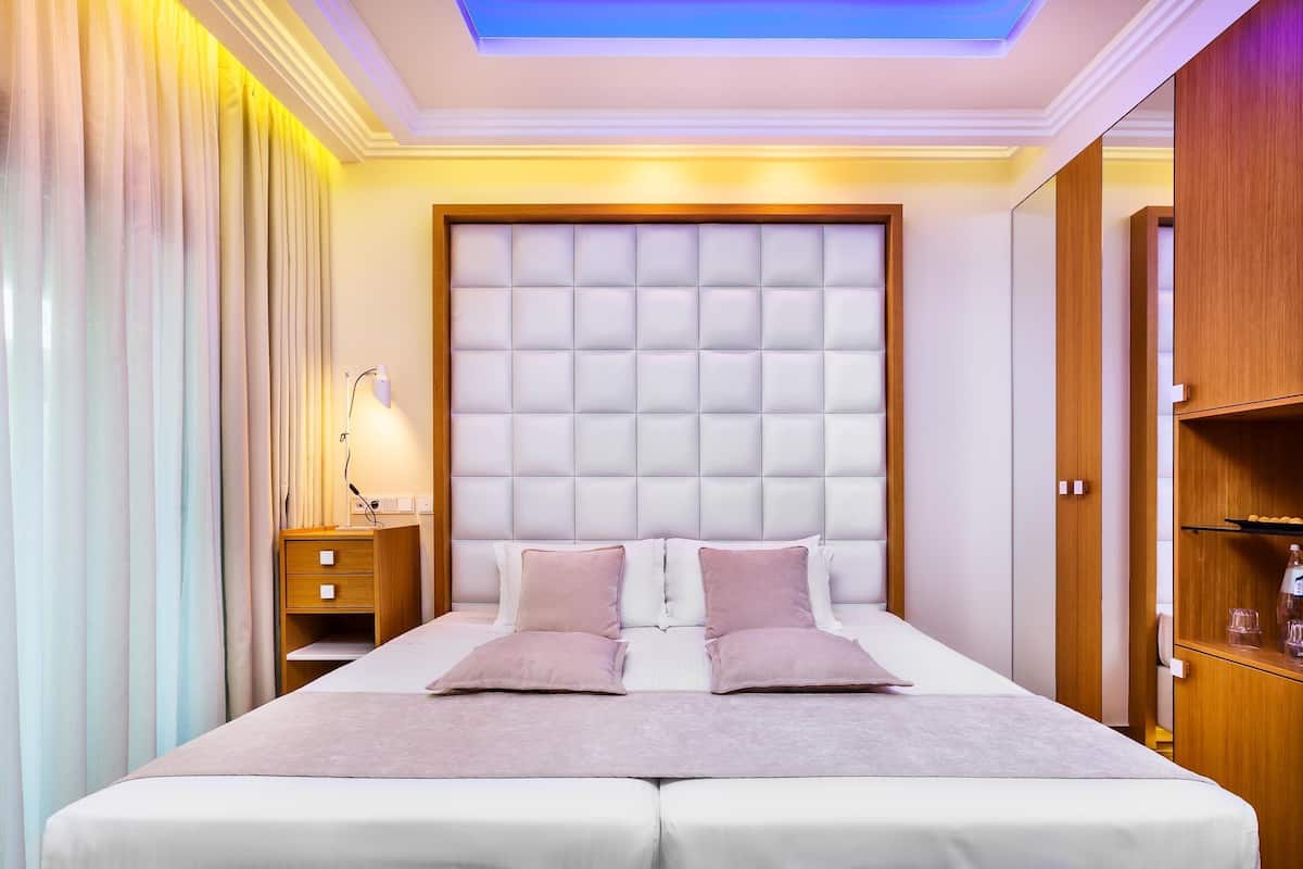 A hotel room with a large bed, a wooden wardrobe, and a bedside table with a lamp.
