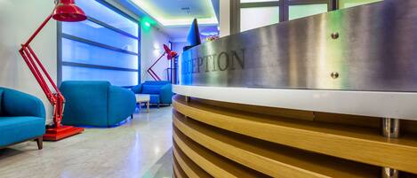A reception area with a modern design, featuring a reception desk, blue sofas, and red floor lamps.