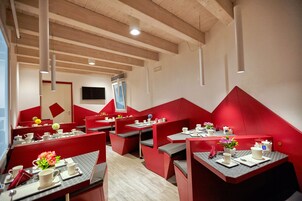 Un ristorante moderno con sedute rosse e tavoli bianchi, caratterizzato da un soffitto in legno e un'ampia vetrata.