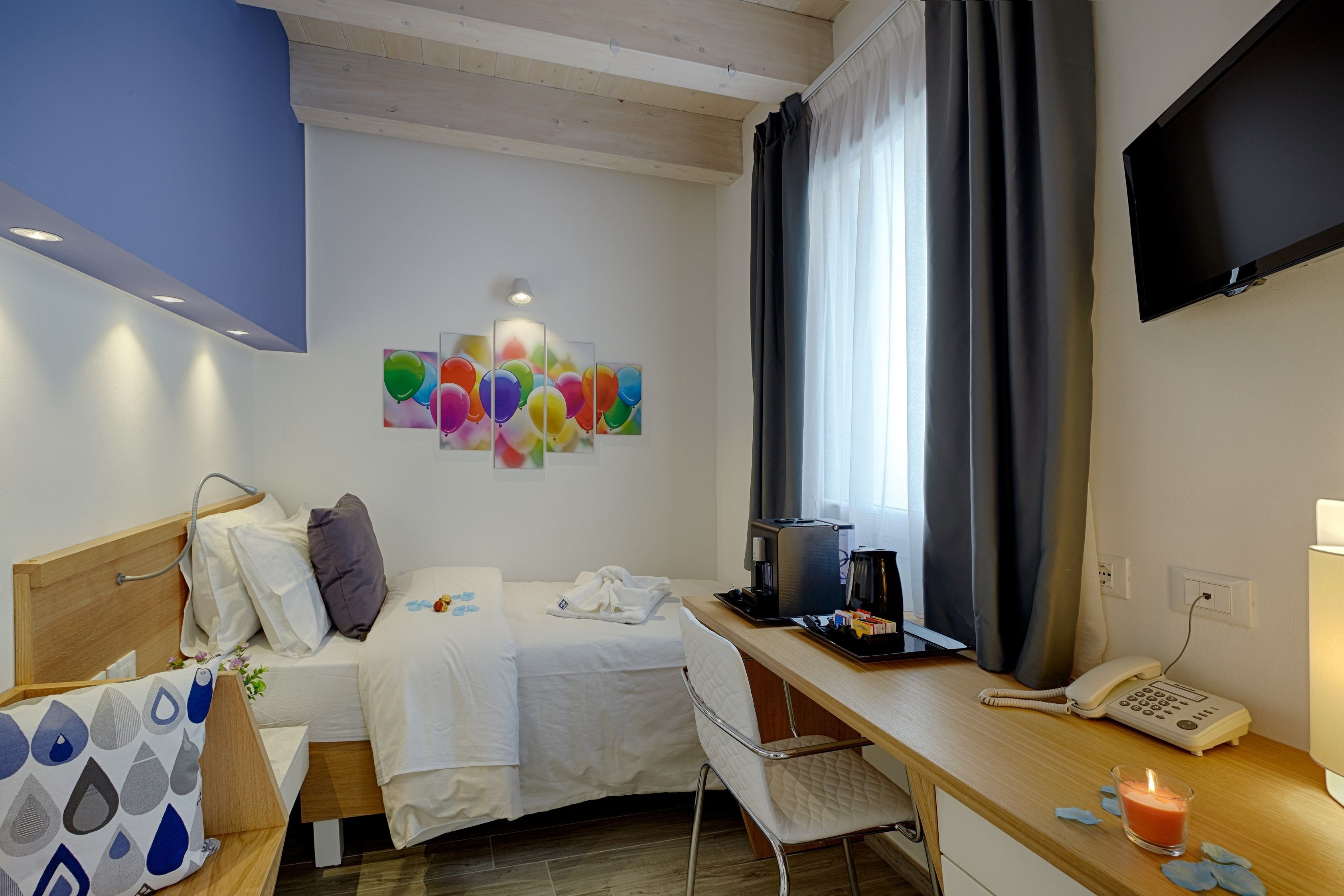 A hotel room with a bed, a desk with a coffee maker, a phone, and a TV on the wall.