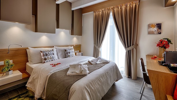 Ein Hotelzimmer mit einem großen Bett, einem Schreibtisch mit Computer und einem Fenster mit Vorhängen.