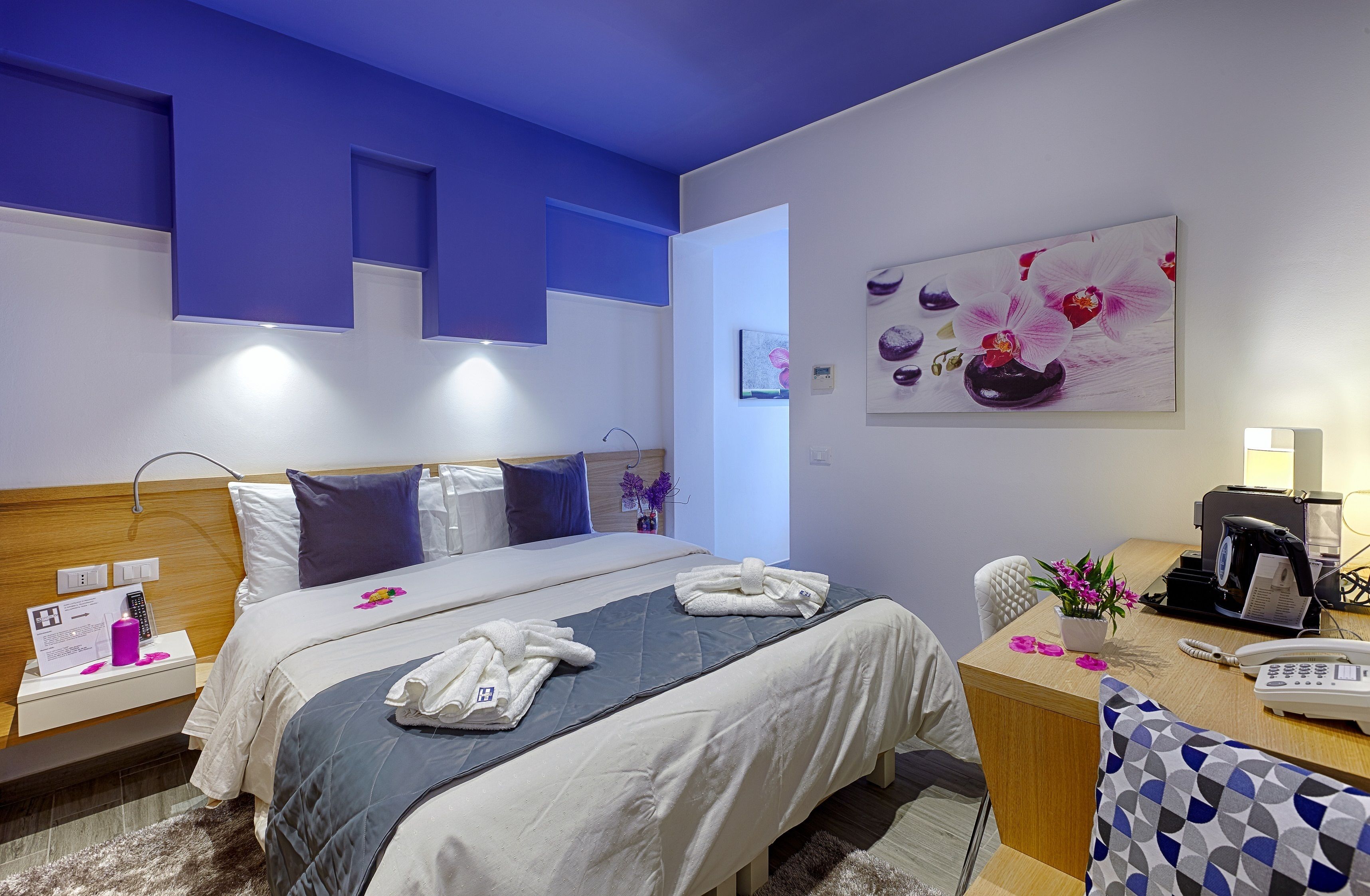 Une chambre d’hôtel avec un lit, une table de chevet, un bureau et un tableau représentant des fleurs.