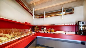 Ein Frühstücksbuffet mit einem roten Tresen, einer Kaffeemaschine und verschiedenen Speisen.
