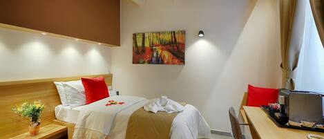 A hotel room with a bed, a desk, a chair, a red rug, a plant, and a painting on the wall.