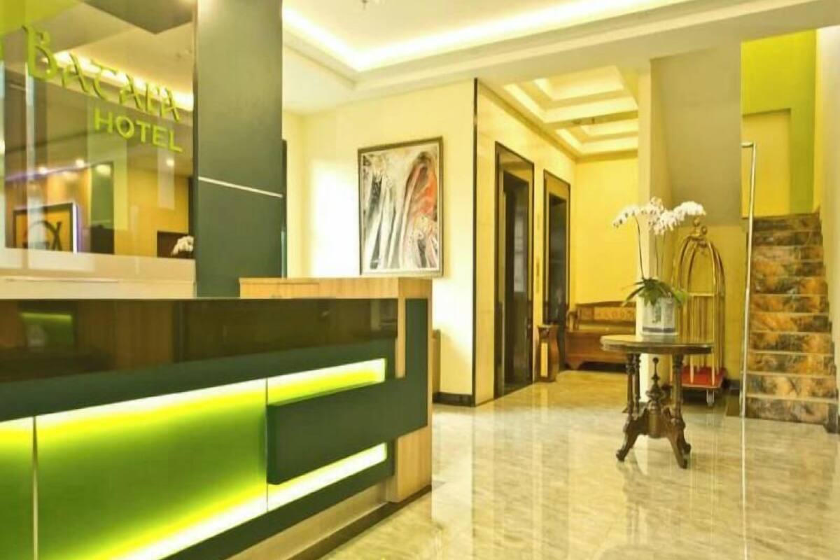 A hotel reception area with a reception desk, a staircase, and a potted plant.