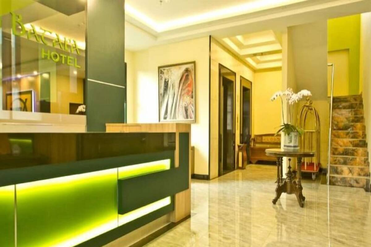 A hotel reception area with a reception desk, a staircase, and a potted plant.