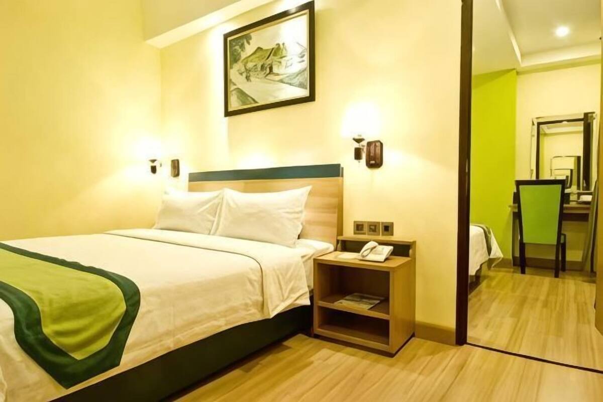 A hotel room with a bed, bedside table, and a mirror.