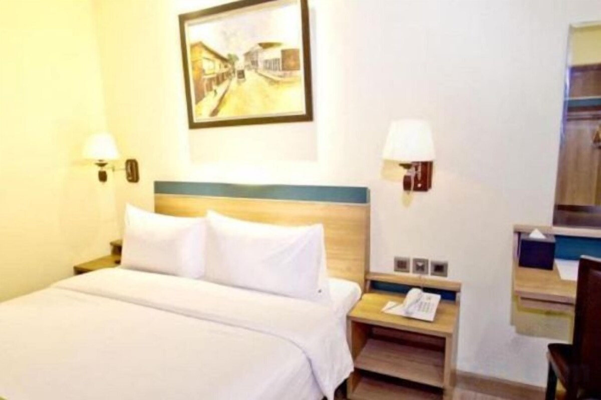 Habitación de hotel con cama, lámparas de noche, mesita de noche y un cuadro en la pared.
