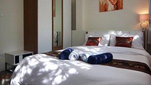 A neatly made bed with rolled towels, a wardrobe, a painting on the wall, and a bedside lamp. - Villa Avalon (Ko Pha-ngan)