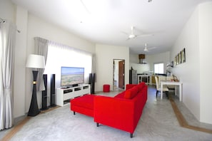 A modern living room with a red sofa, a flat-screen TV, and a dining area with a white table and chairs.