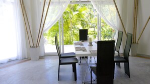 A dining area with a table set for four, large windows with sheer curtains, and bamboo sticks placed on either side of the windows. - Villa Avalon (Ko Pha-ngan)