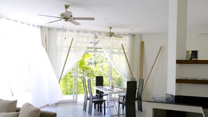 A modern dining area with a table and chairs, a ceiling fan, and a view of greenery outside. - Villa Avalon (Ko Pha-ngan)
