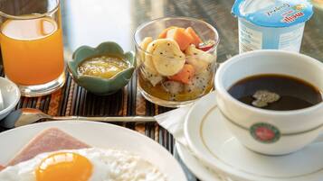 Un desayuno con tostadas, un huevo, un vaso de jugo de naranja, un frutero, una taza de café y un recipiente con yogur.