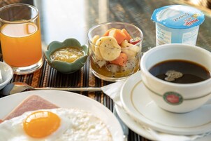 Un desayuno con tostadas, un huevo, un vaso de jugo de naranja, un frutero, una taza de café y un recipiente con yogur.