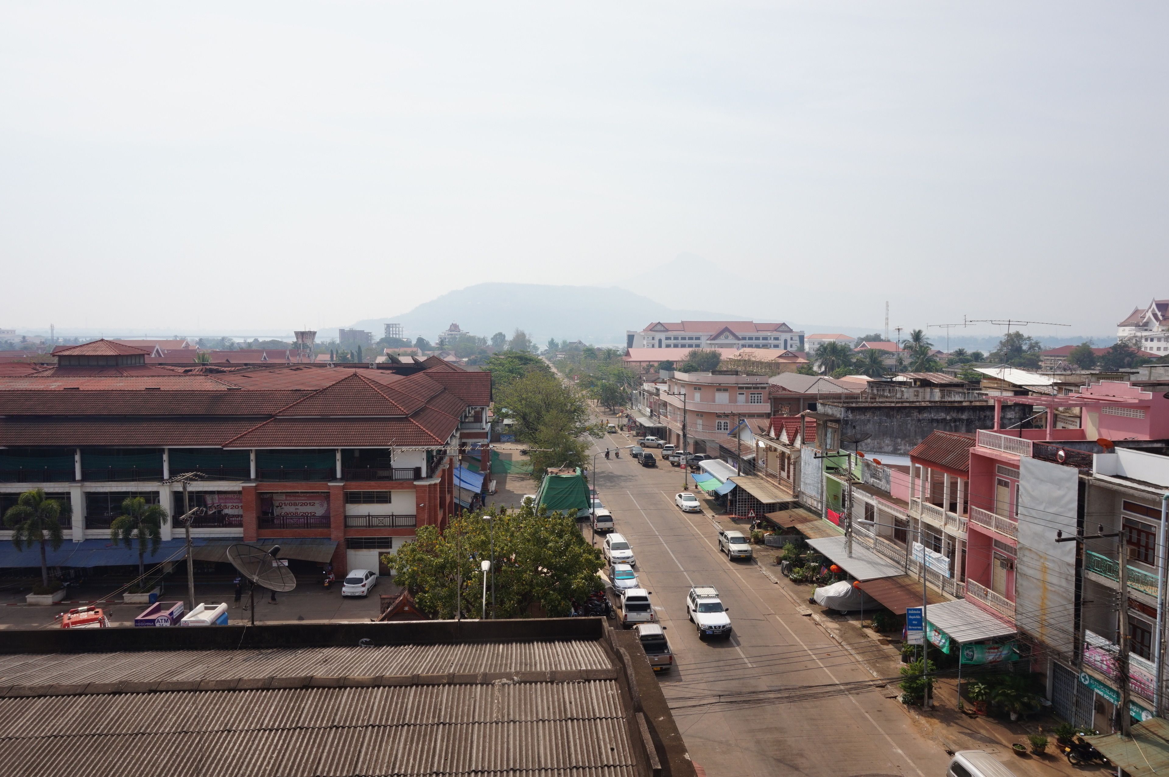 A street view with buildings, parked cars, and a distant mountain.