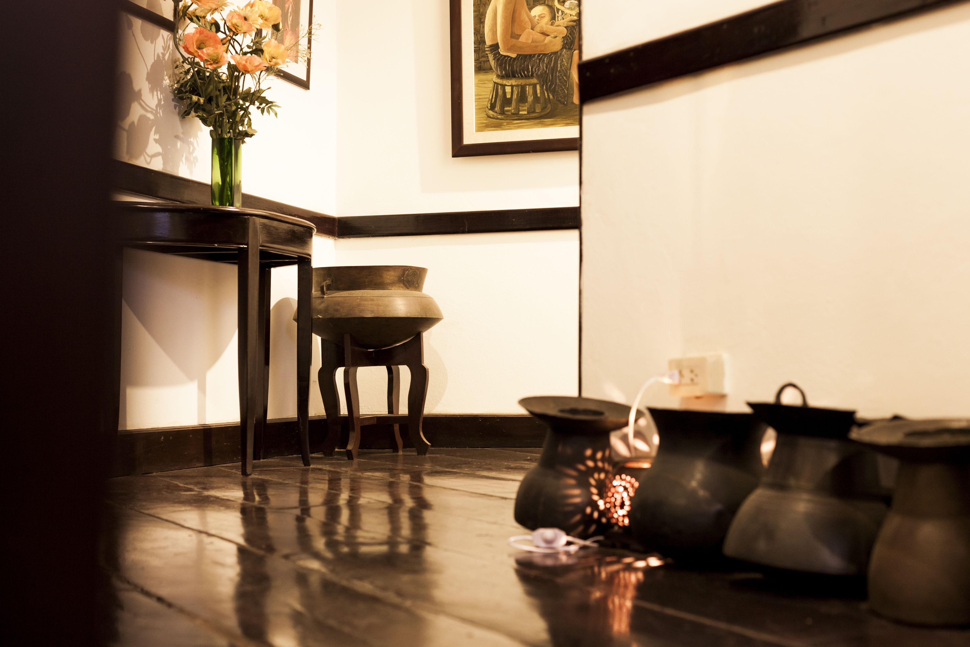 Una cocina tradicional con una mesa de madera, un jarrón de flores y varias ollas y sartenes en el suelo.