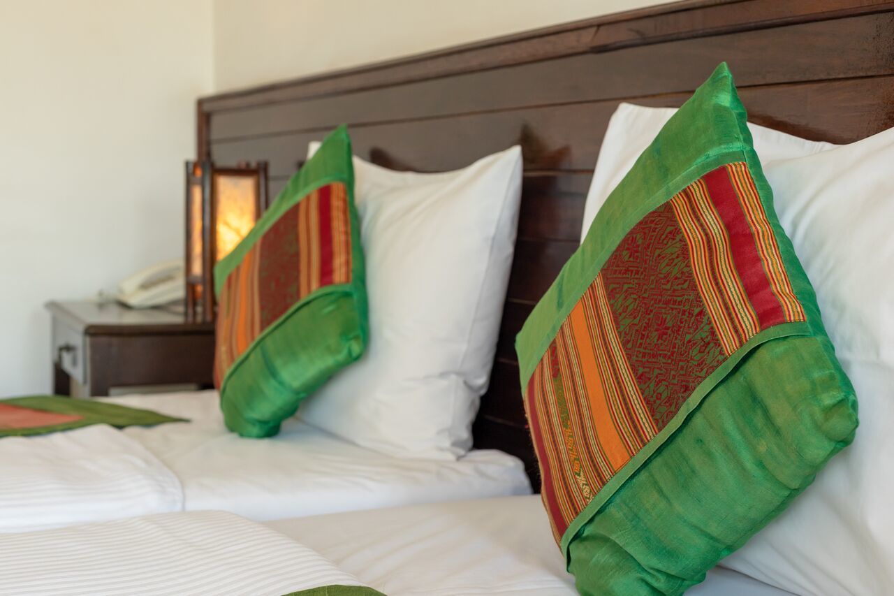 Une chambre d’hôtel avec un lit bien fait, deux oreillers aux motifs verts et rouges, et une table de chevet avec une lampe et un téléphone.