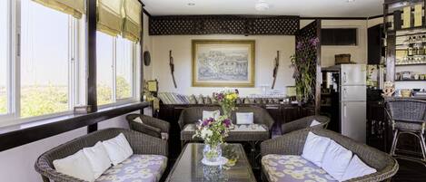 A dining area with wicker furniture, a glass table, and a painting on the wall.