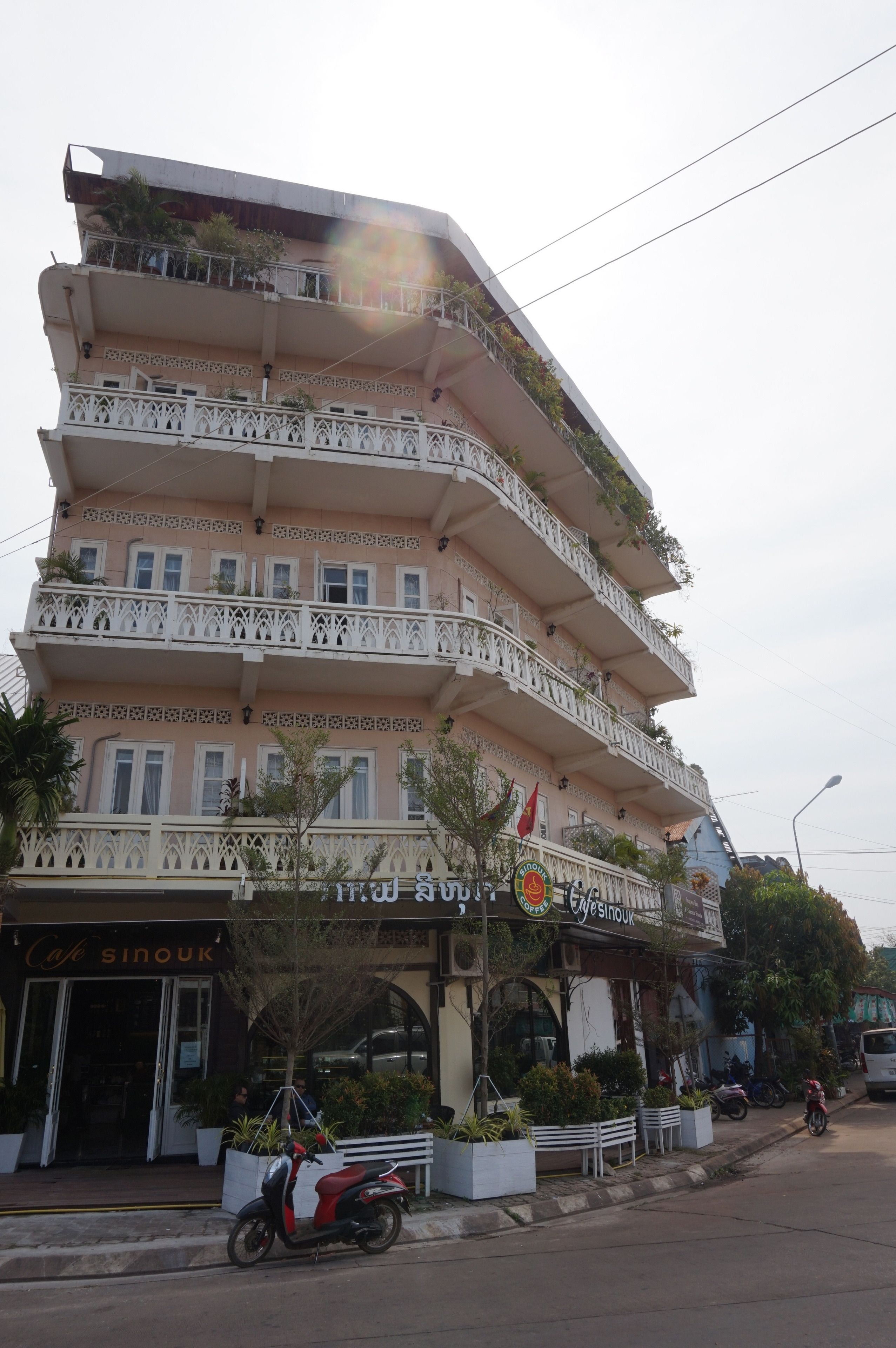 A multi-story building with balconies, a cafe named 'Cafe Sinouk' at the ground level, and a sign for 'Yesinou'.