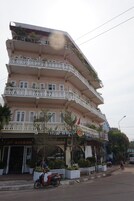 Un edificio de varios pisos con balcones, una cafetería llamada 'Cafe Sinouk' en la planta baja y un letrero que dice 'Yesinou'.