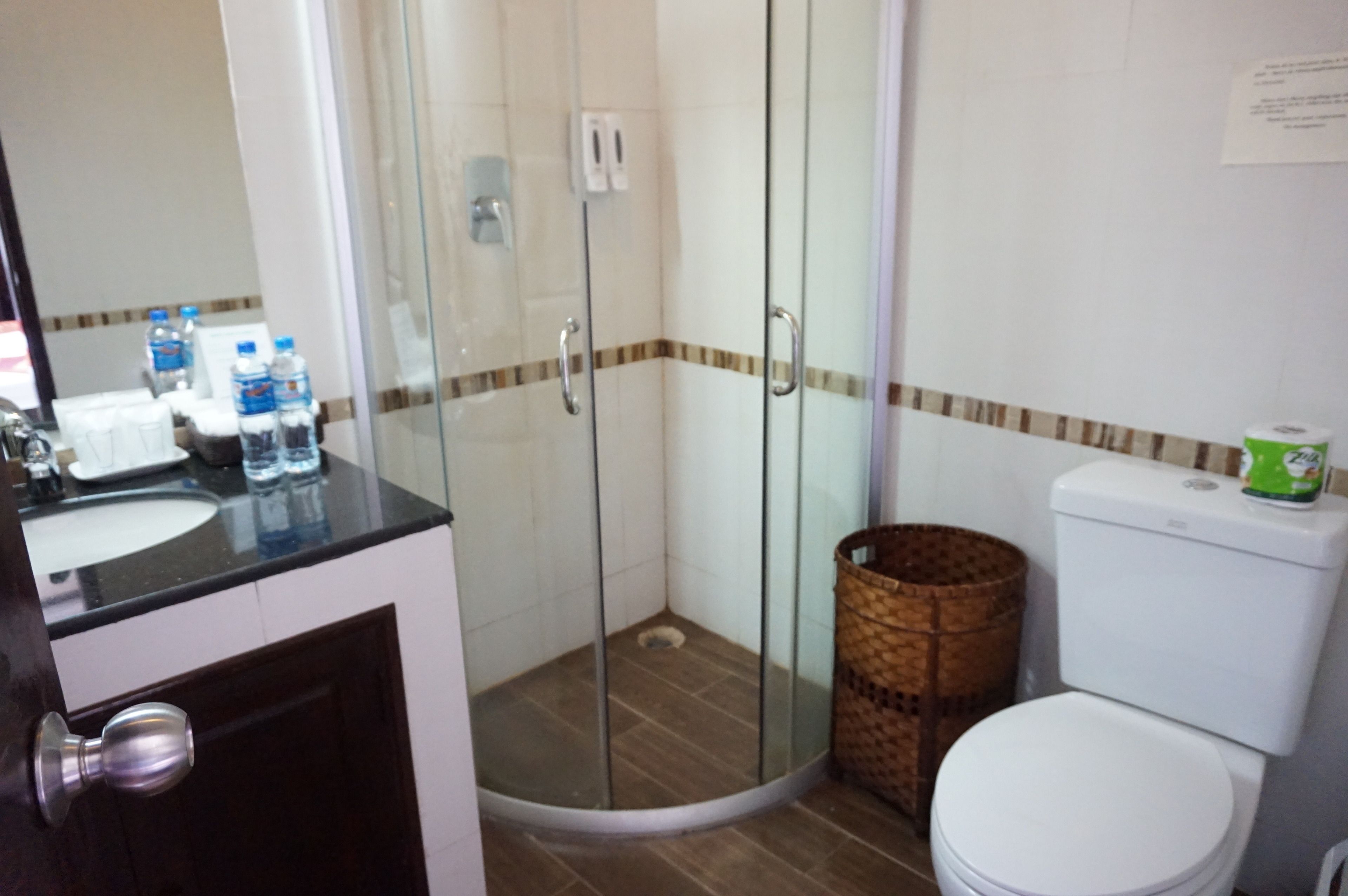 A bathroom with a glass-enclosed shower, a toilet, and a sink with bottled water.