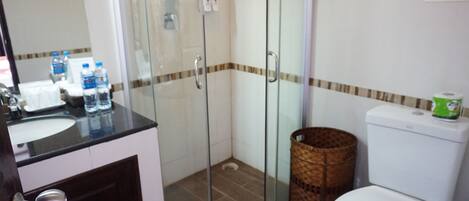 A bathroom with a glass-enclosed shower, a toilet, and a sink with bottled water.