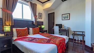 A well-lit hotel room with a large bed, bedside tables, a desk, and a chair.