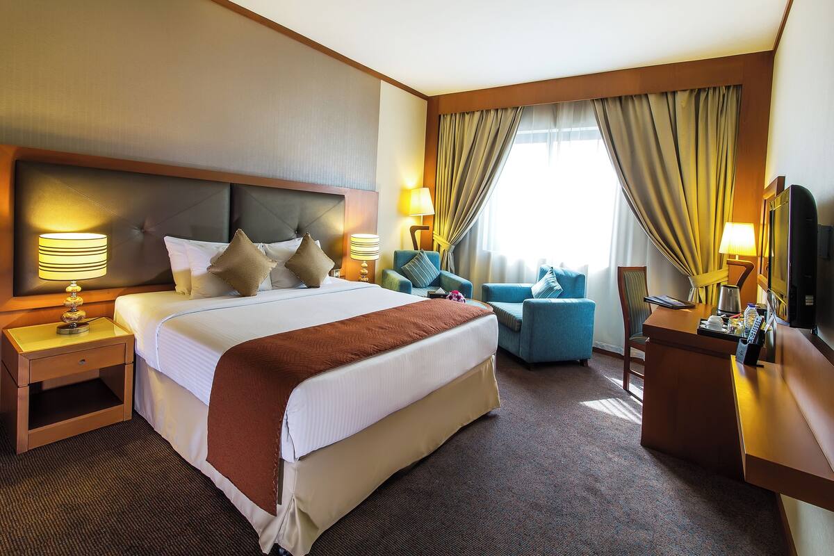 A hotel room with a large bed, two bedside tables, a desk, and a chair.