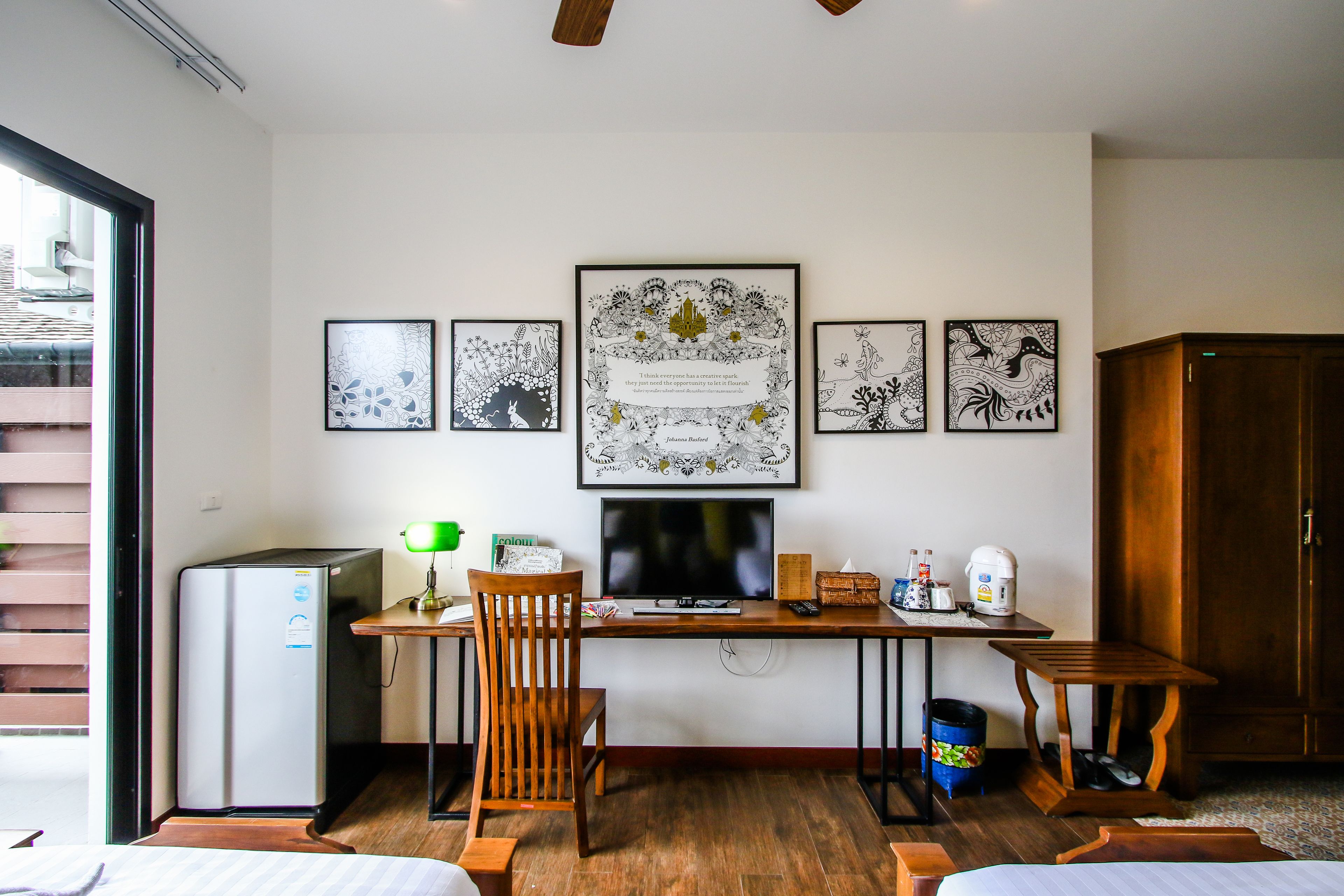 A compact hotel room with a wooden desk, a small refrigerator, a TV, and a bed.