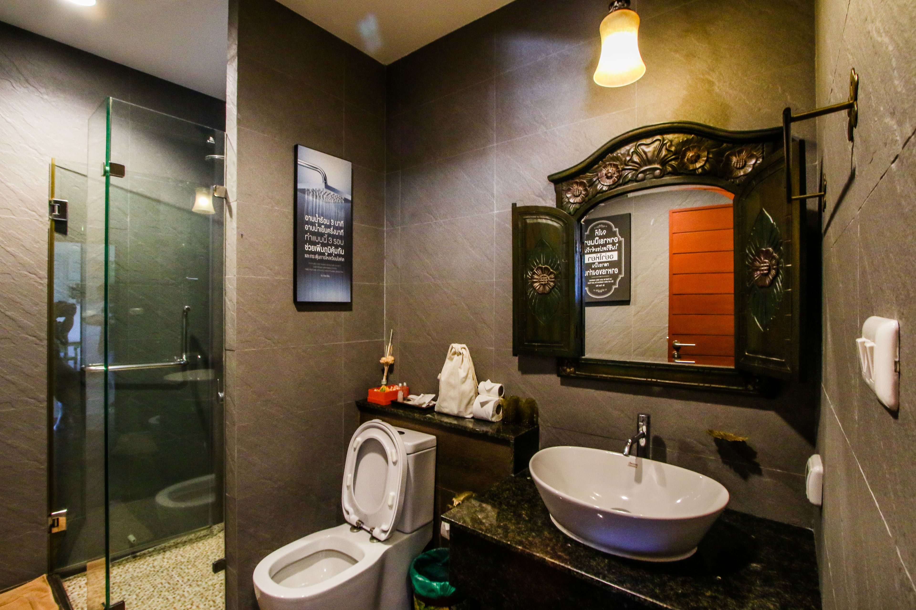 A modern bathroom with a glass shower enclosure, a toilet, a sink with a marble countertop, and a decorative mirror with an ornate frame.