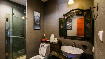 A modern bathroom with a glass shower enclosure, a toilet, a sink with a marble countertop, and a decorative mirror with an ornate frame.