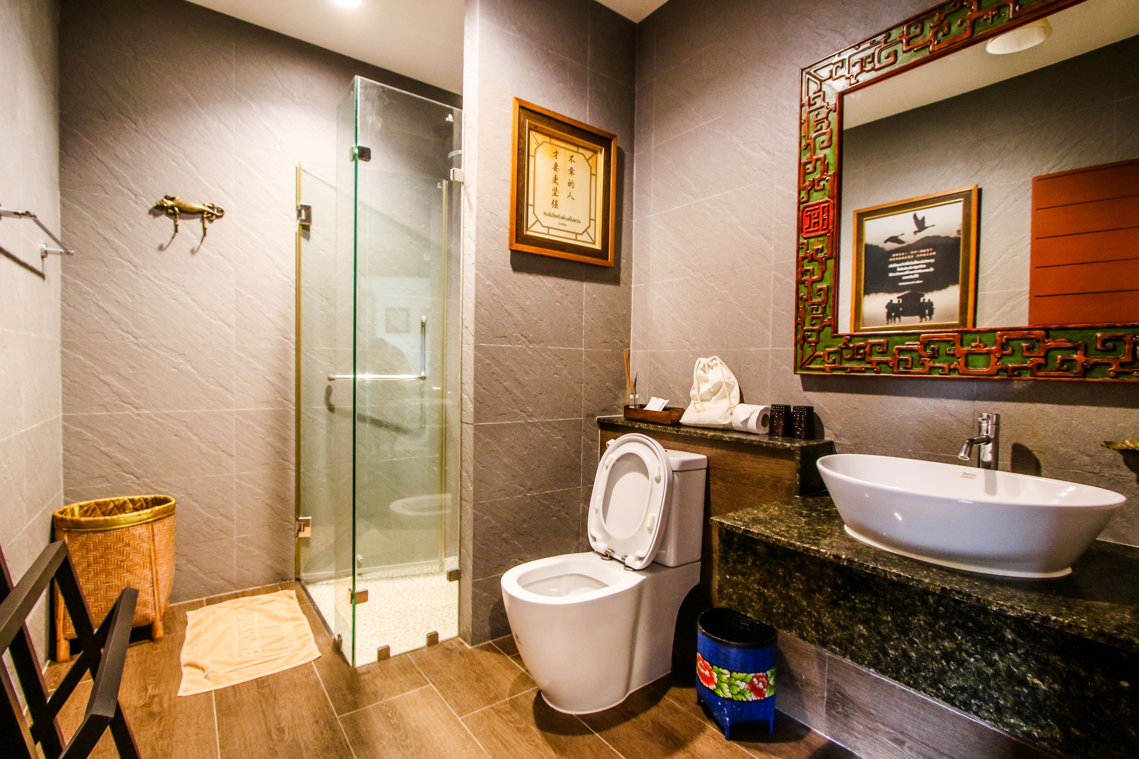 A bathroom with a glass shower enclosure, a toilet, a sink, and a mirror with a decorative frame.