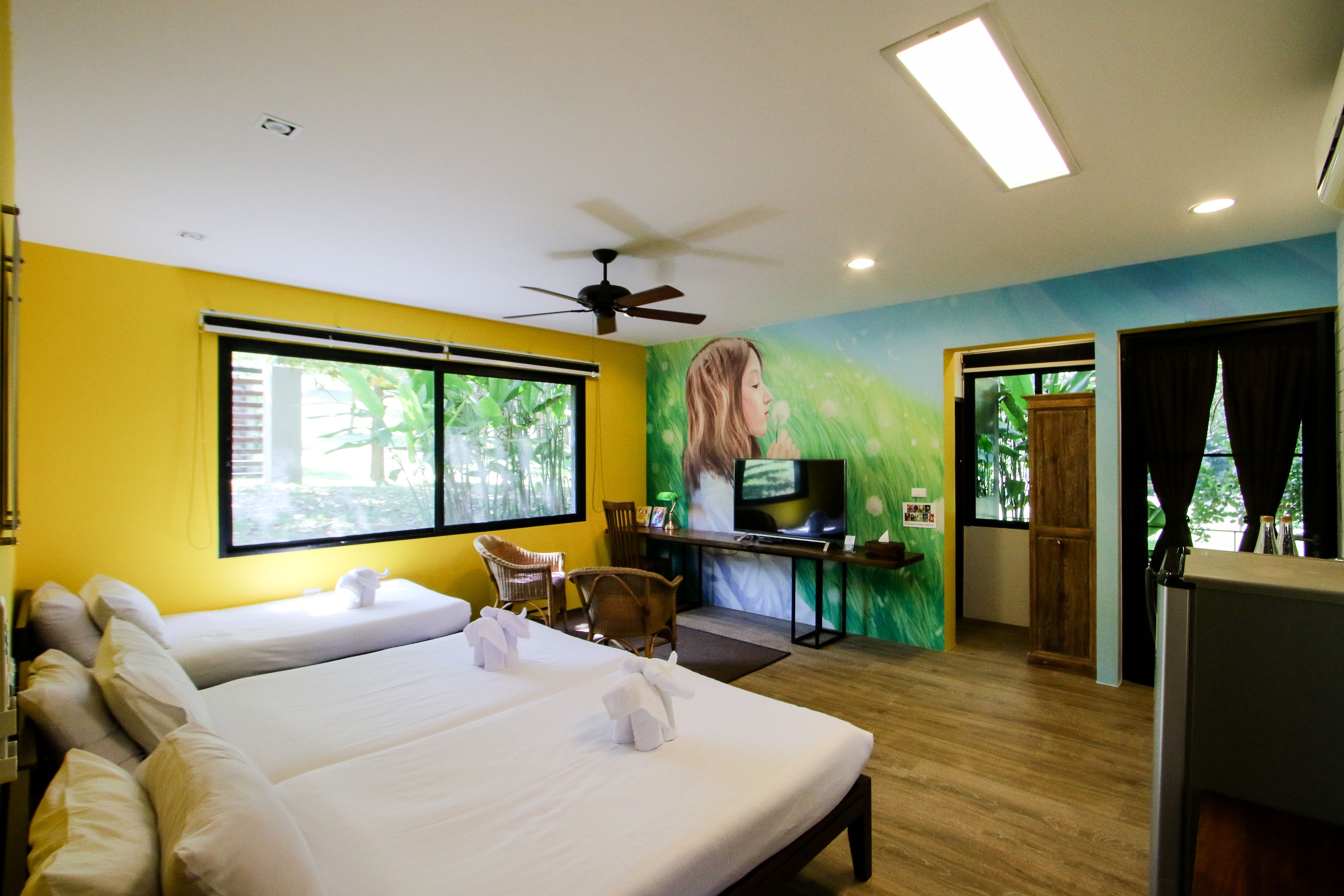 Habitación de hotel con dos camas, televisión, escritorio y ventilador de techo.