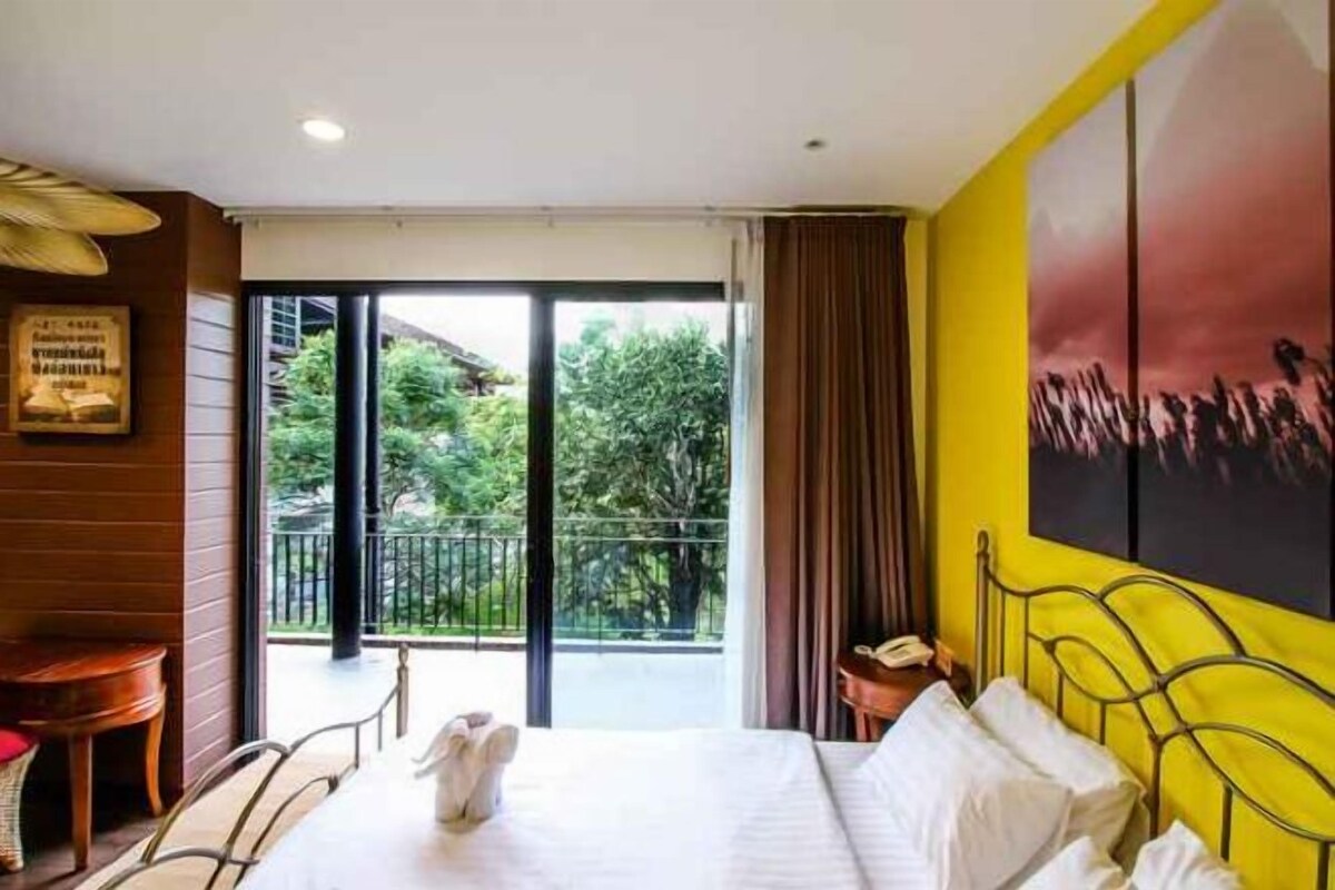 Habitación de hotel con cama, una silla, una mesa y un balcón con vistas a árboles.