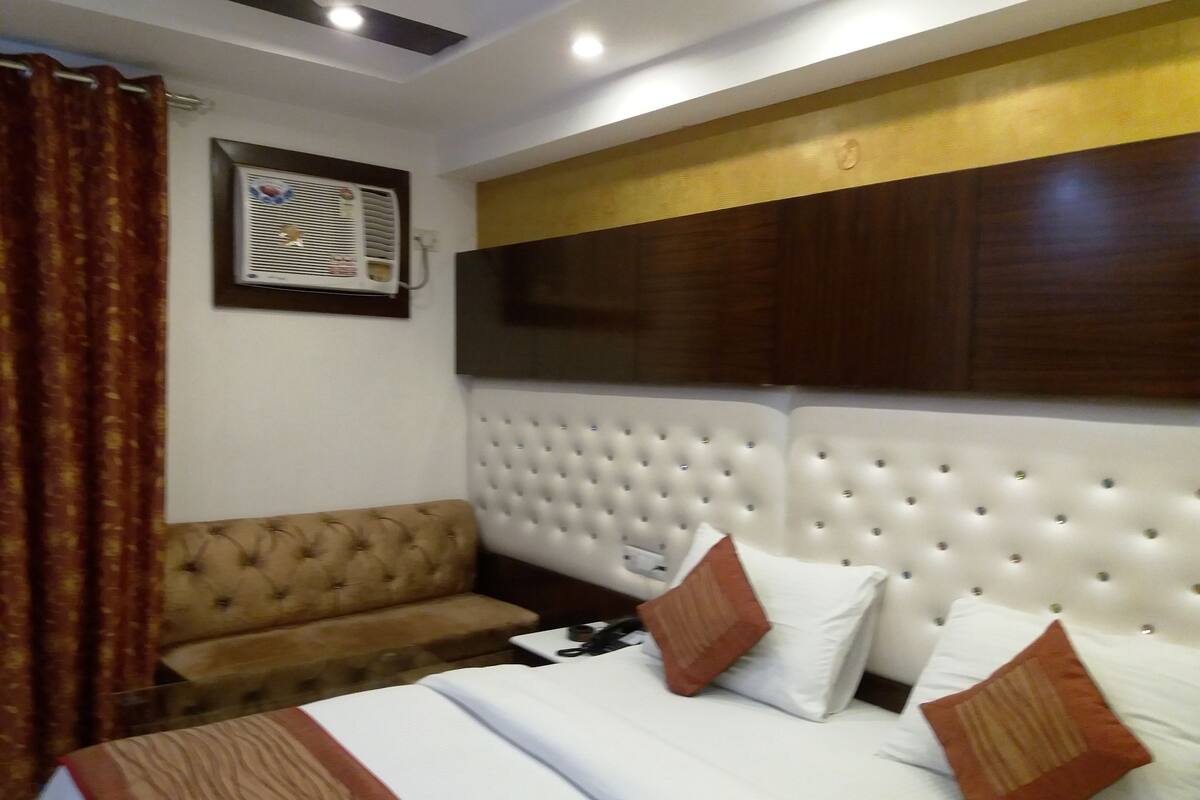 A hotel room with a large bed, a sofa, and a wall-mounted air conditioner.