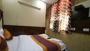 A neatly made bed with white and yellow bedding, a flat-screen TV mounted on the wall, and a power outlet on the wall. - Lord Krishna Hotel Dx. Inn (New Delhi)