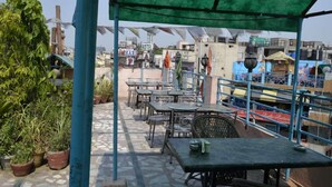 An outdoor seating area with tables and chairs, surrounded by potted plants and a green canopy. - Lord Krishna Hotel Dx. Inn (New Delhi)
