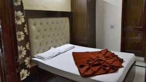 A single bed with a white mattress and a brown blanket, a tufted headboard, and a floral-patterned curtain. - Lord Krishna Hotel Dx. Inn (New Delhi)